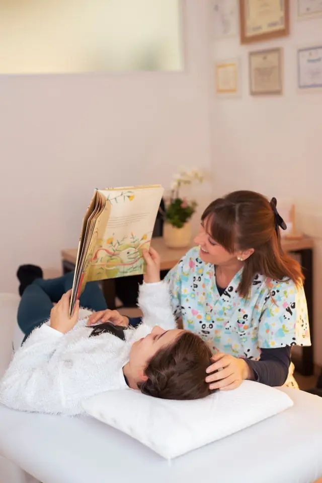 Giulia legge un libro illustrato a una bambina sdraiata sul lettino
