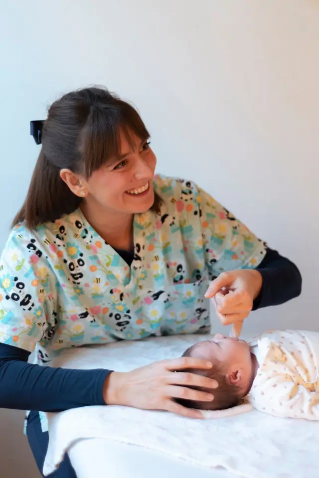 Giulia sorride mentre tratta con delicatezza la testa di un neonato