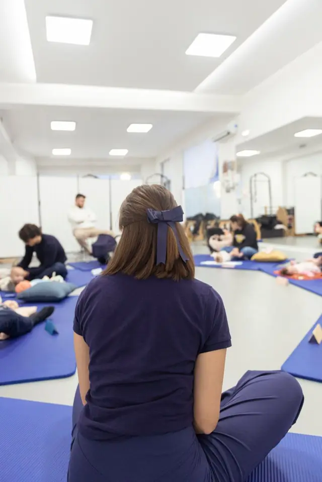 Sala luminosa con più famiglie sui tappetini durante il corso